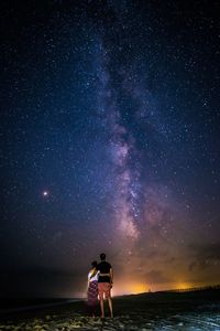 Rear view of woman standing on field against sky at night