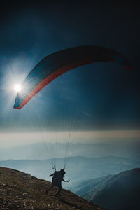 Person paragliding over mountains against sky