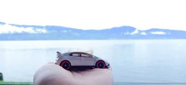 Close-up of hand holding car against sea