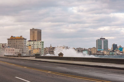 Road passing through city against cloudy sky