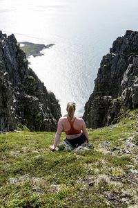 Rear view of woman sitting on cliff