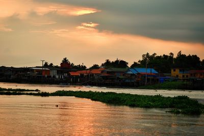 Houses by river against sky during sunset