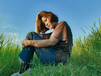 Young woman sitting on field against sky