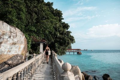 Rear view of woman standing by sea against sky