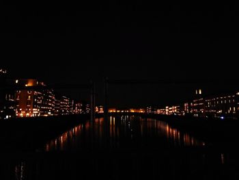 Illuminated city by river against sky at night