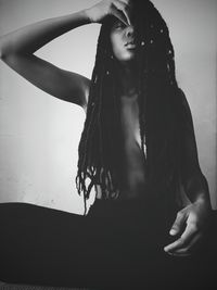 Topless young woman with dreadlocks sitting against wall