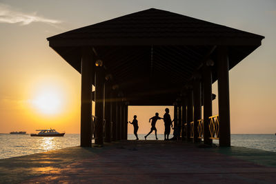 Silhouette boys in gazebo by sea during sunset