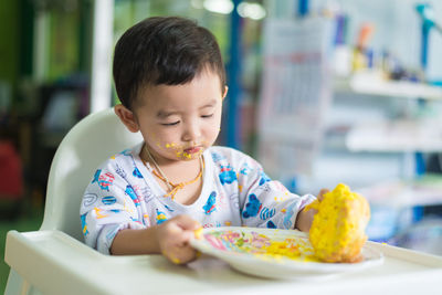 Boy with messy face sitting by food in plate on table