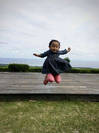 Full length of girl jumping on grass against sky