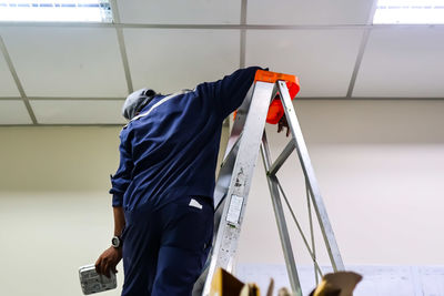 Rear view of man repairing ceiling
