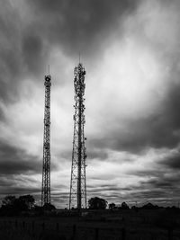Low angle view of two communication towers against cloudy sky