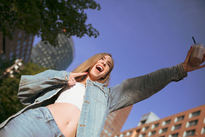 Low angle view of excited woman holding disposable cup in city