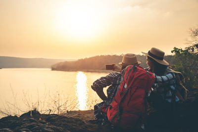 Rear view of people looking at lake against sky during sunset