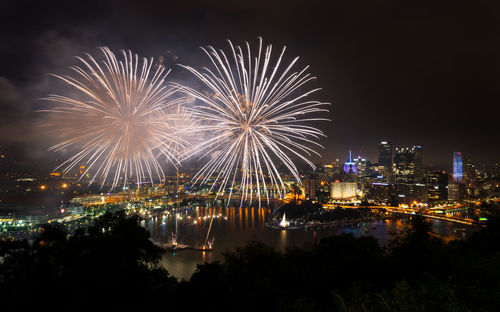 Firework display in city against sky at night