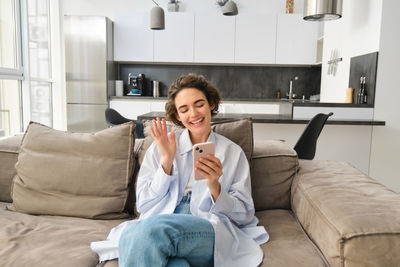 Young woman using mobile phone while sitting on sofa at home