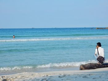 Rear view of photographer photographing man swimming in sea