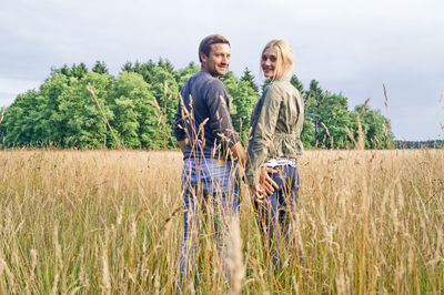 Portrait of man and woman standing on grassy field against sky