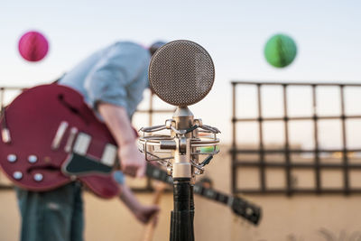 Close-up of microphone with man standing with guitar standing outdoors