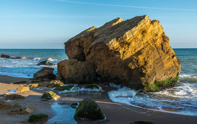 Rocks on beach by sea against sky