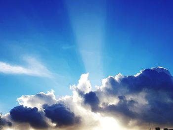 Low angle view of sunlight streaming through clouds