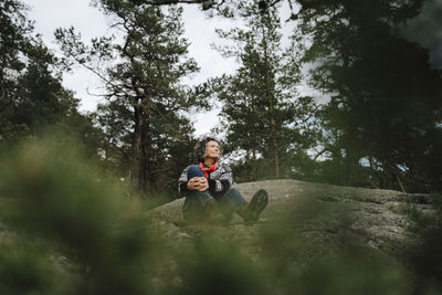 Mature woman sitting on mountain amidst tree in forest