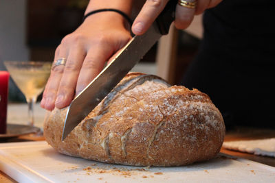 Cropped hands cutting bread on table