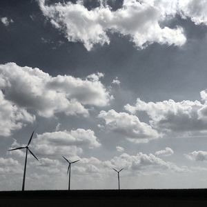 Wind turbines on field against cloudy sky