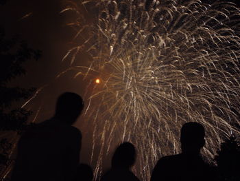 Silhouette people looking at fireworks explosion against sky