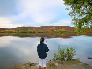 Rear view of man standing by lake against sky