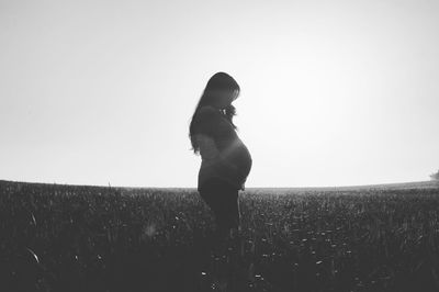 Pregnant woman standing on field against sky during sunny day