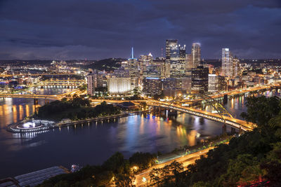 Illuminated buildings by river in city at night