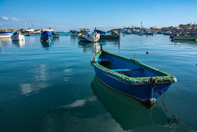 Fishing boats moored in sea against blue sky