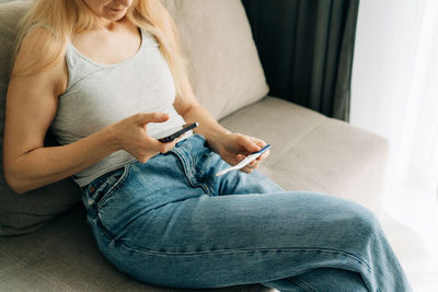 Unrecognizable woman with pregnancy test and mobile phone on sofa at home.