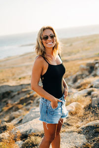 Portrait of happy woman wearing sunglasses while standing on beach