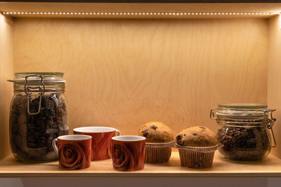 Muffins, cups of coffee and glass jars containing coffee and cocoa, breakfast theme.