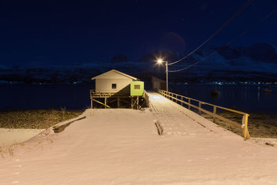 Snow covered pier by lake against sky at night