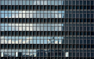 Glass curtain wall facade of a generic modern office building, with the sky reflected on its surface