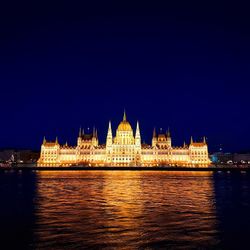 Illuminated building over river in city against sky at night