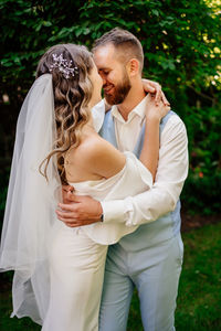Newlywed couple embracing against trees