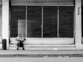 Man checking his bag while sitting against closed shutter