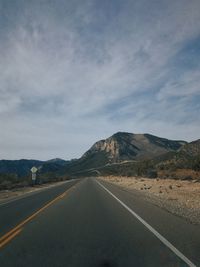 Empty road by mountains against sky