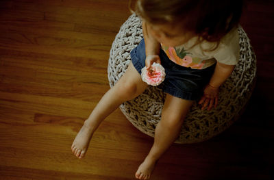 Young girl sitting on a puff holding a pink flower in her living room