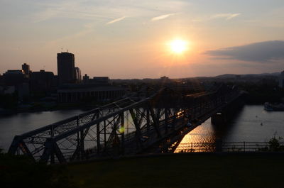 Silhouette bridge over river against sky during sunset in city