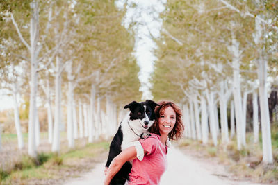 Portrait of woman carrying dog while standing in forest