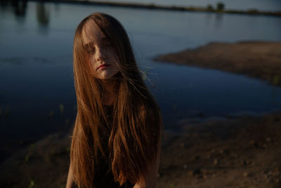 Portrait of a beautiful young woman standing at lake