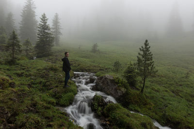 Side view of woman standing by stream during foggy weather