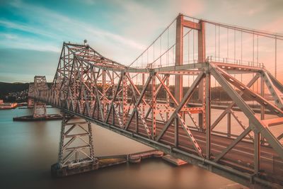 Suspension bridge over river in city against sky