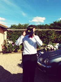 Man photographing with mobile phone while standing against sky
