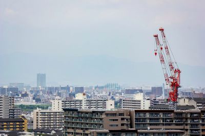 Crane by buildings against sky in city