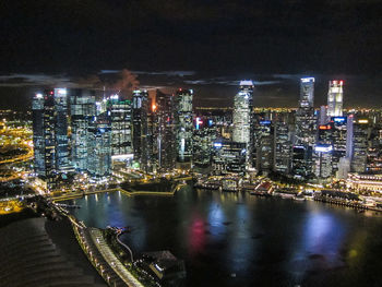 Illuminated buildings by river against sky at night